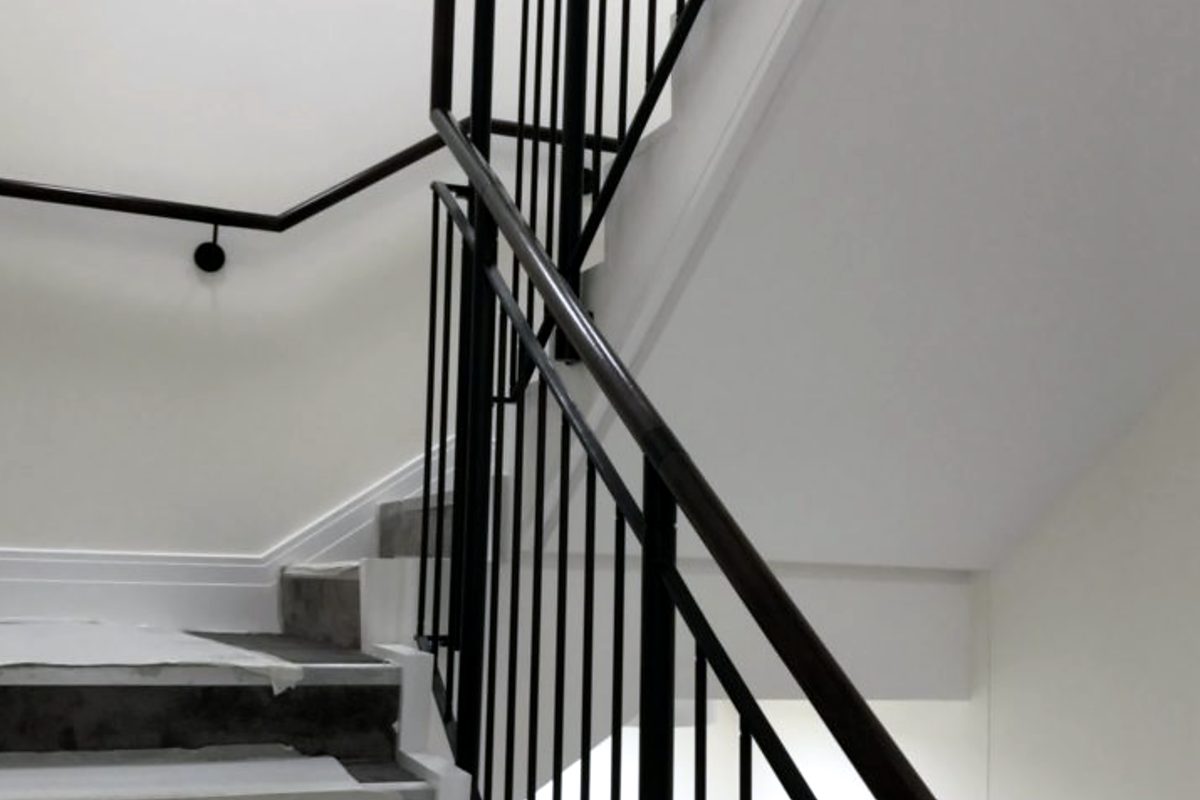 Black steel vertical bar balustrade and handrail on a concrete stair, with a wall handrail on the landing