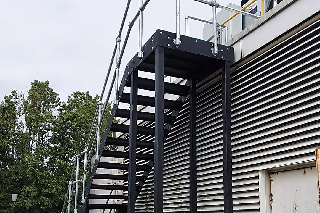 Black steel external stair with galvanised tube handrails up to a roof plant deck on a commercial building