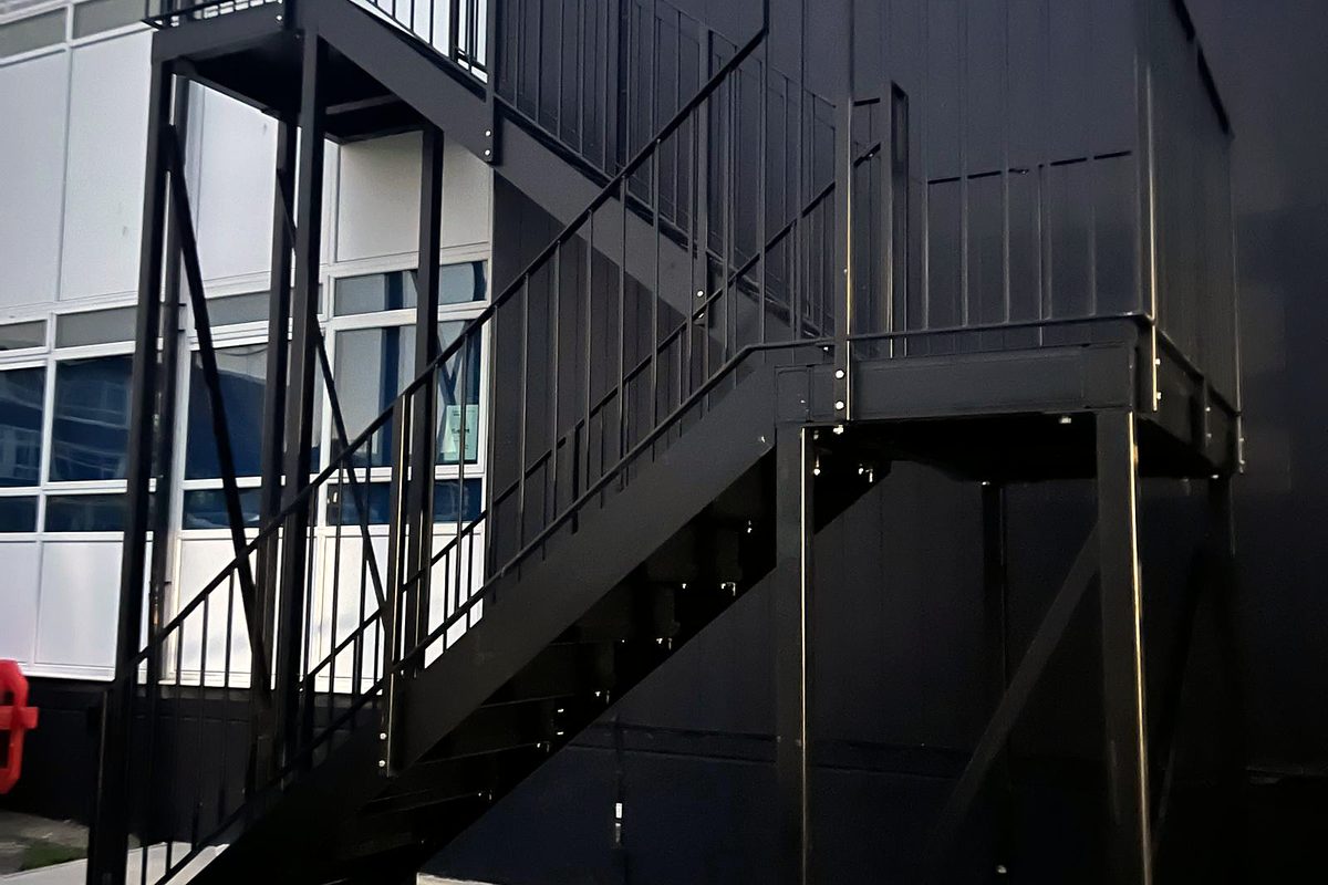 Black steel external stair with two landings and bar railings against a clad commercial building