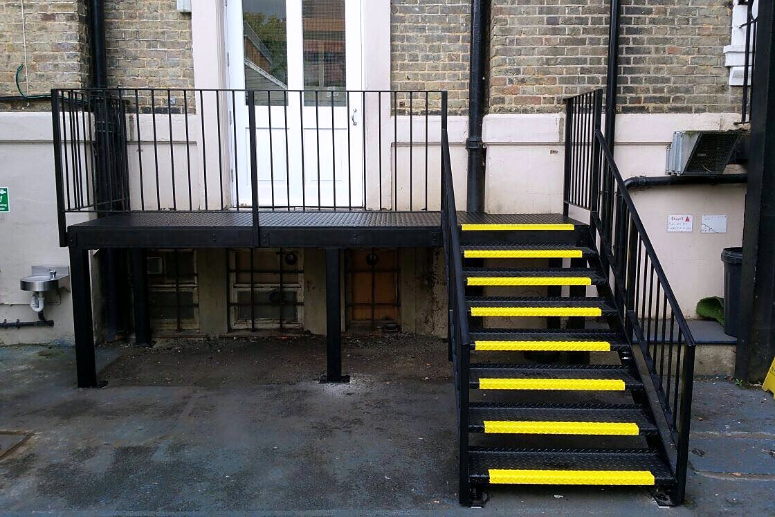 Black steel platform and stair with yellow anti-slip nosings at the back of a building