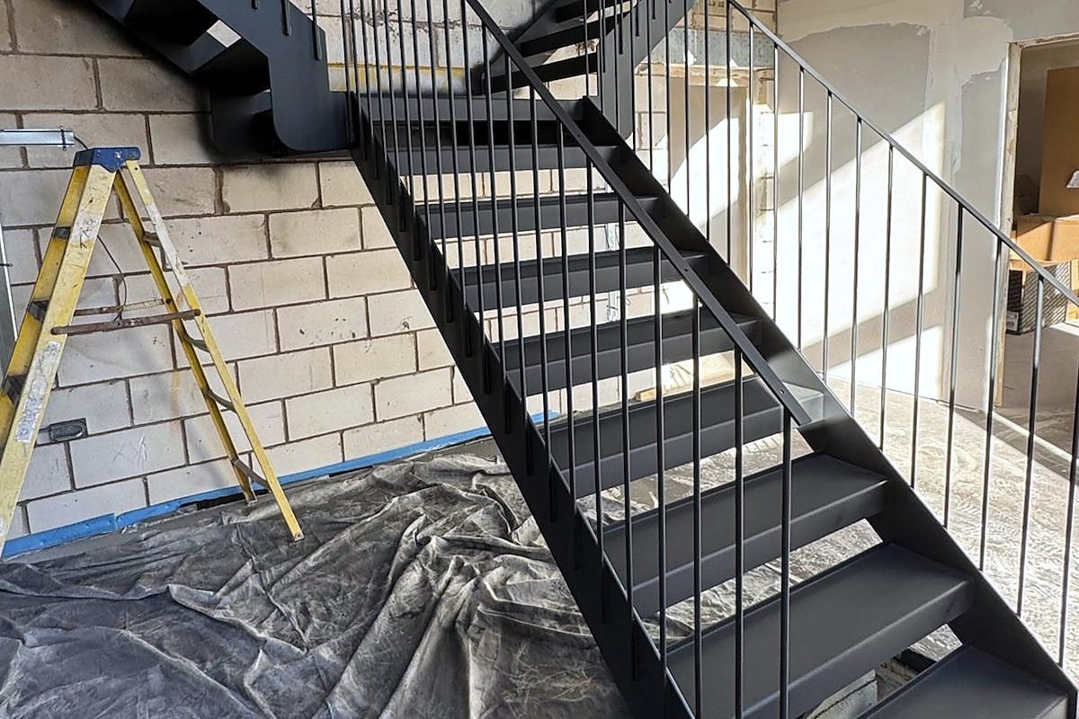 Black steel staircase with a vertical bar balustrade, fitted while the building around it was still being finished
