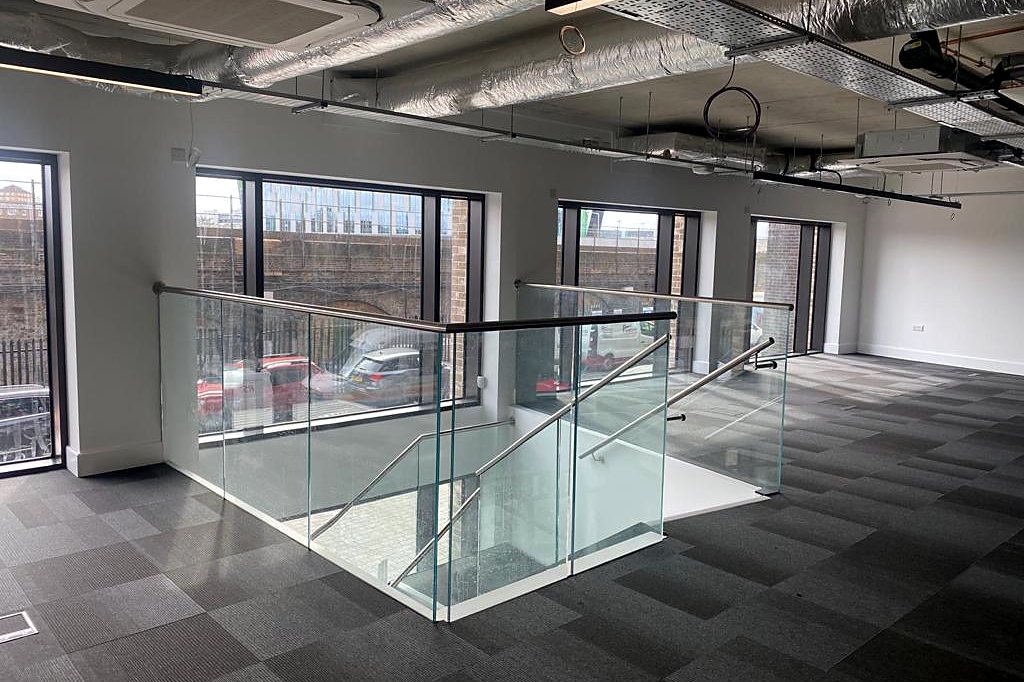 Frameless glass balustrade with a stainless steel handrail around a stair opening in an office