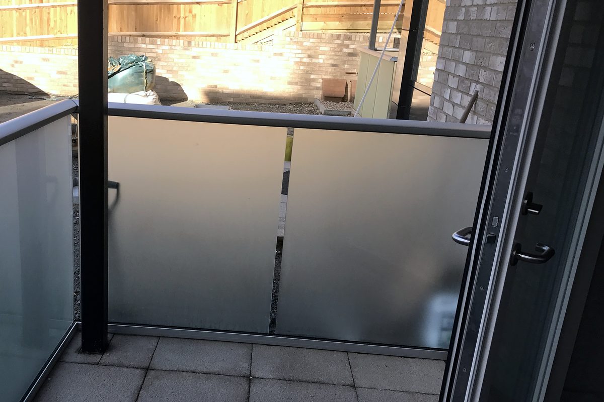 Frosted glass balustrade with a grey top rail around a paved ground-floor terrace outside a block of flats