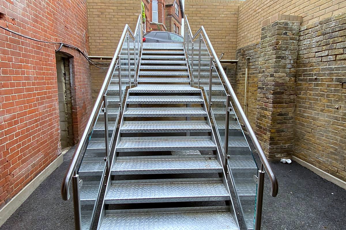 Galvanised chequer plate steel stair with stainless steel handrails between brick walls