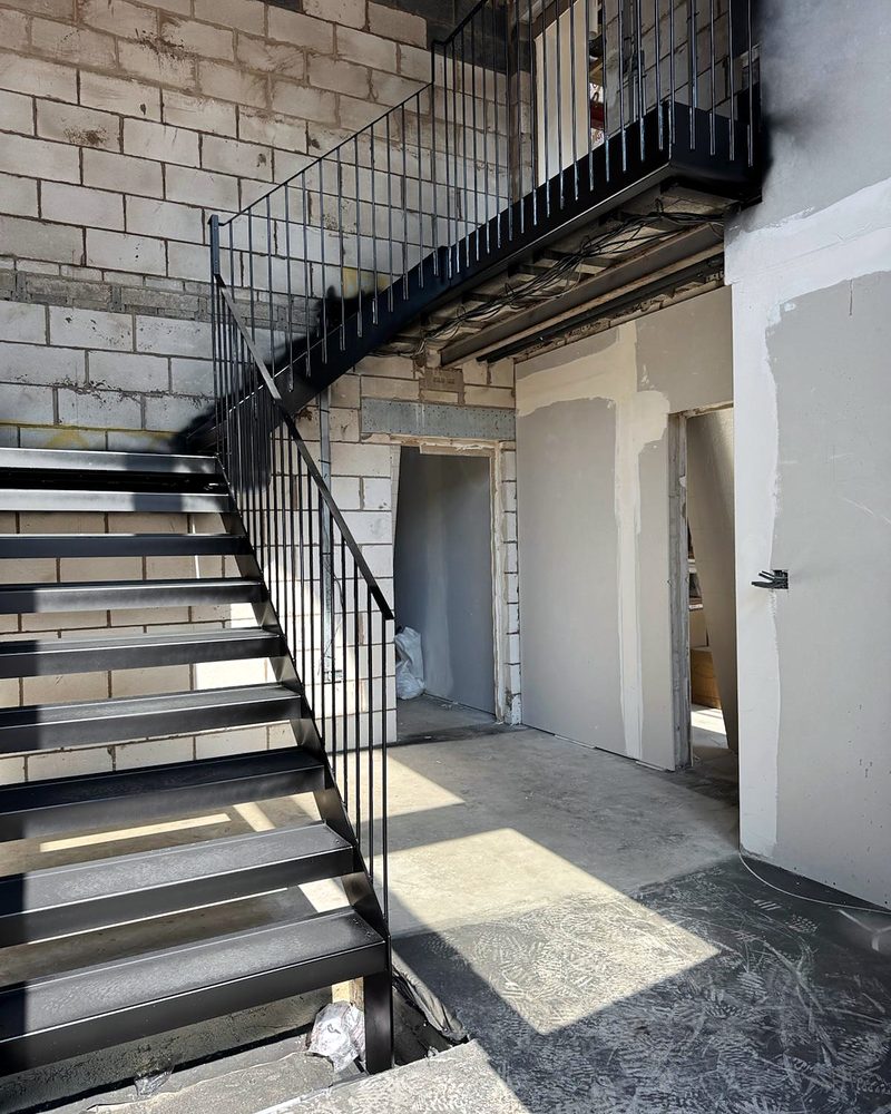 Black steel staircase and landing with a slim bar balustrade, fitted while the building was still being finished