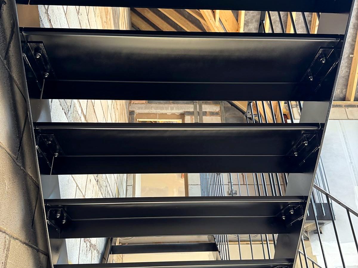 Underside of a black steel staircase, showing the bolted brackets that carry each tread