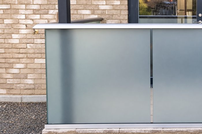 Frosted glass balustrade panels with a grey top rail along a ground-floor terrace beside a yellow brick wall