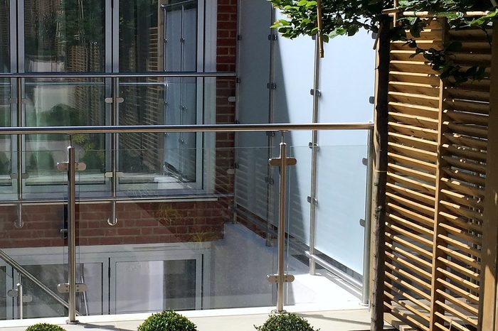 Clear glass panels held by stainless steel posts and handrails around a basement lightwell, with a frosted privacy screen on one side