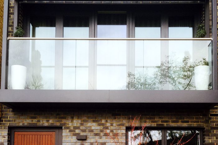 Frameless glass balcony on a grey steel base across a yellow brick townhouse