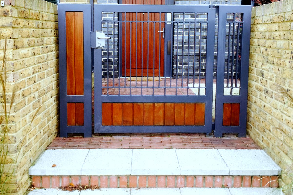 Grey steel pedestrian gate with hardwood panels between yellow brick walls at a house entrance
